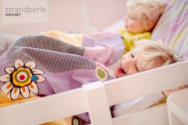 Zwei junge Brüder liegen im Bett  einer lacht.