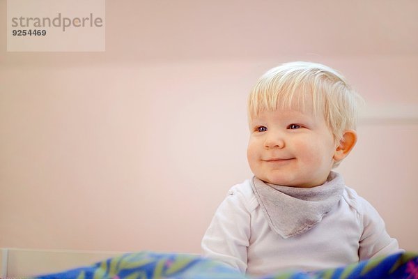 Porträt eines süßen vierzehn Monate alten Jungen  der auf einer Bettdecke sitzt.