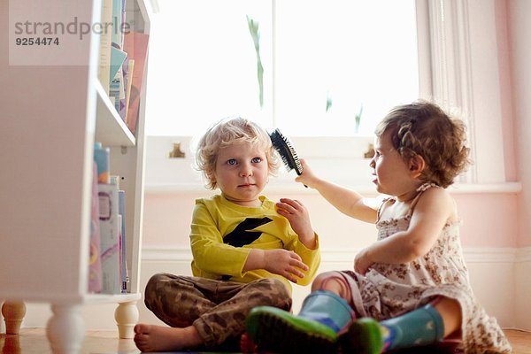Weibliches Kleinkind bürstet männliches Kleinkind Haar im Spielzimmer