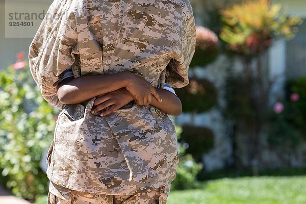 Abgeschnittene Rückansicht einer Soldatin  die ihren Sohn beim Homecoming umarmt.