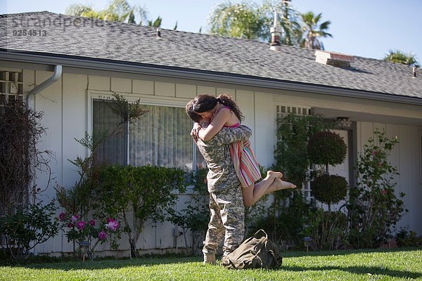 Männlicher Soldat umarmt und hebt Frau im Garten beim Homecoming an.
