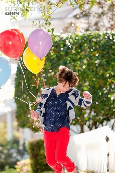 Zehnjähriges Mädchen springt aufgeregt mit einem Haufen Luftballons