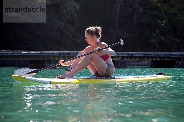 Mittlere erwachsene Frau setzt sich zum Paddeln aufs Meer.