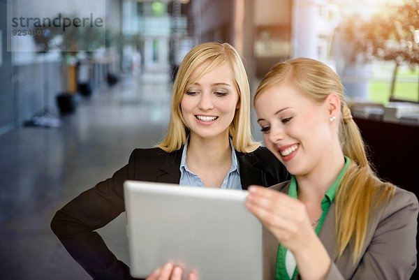 Zwei junge Geschäftsfrauen beim Blick auf das digitale Tablett im Büro