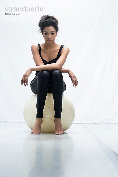 Studio-Porträt einer selbstbewussten jungen Frau  die auf einem Übungsball sitzt.