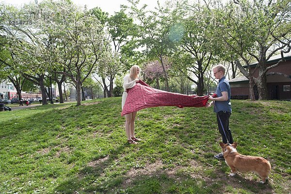 Junges Paar schüttelt Picknickdecke im Park