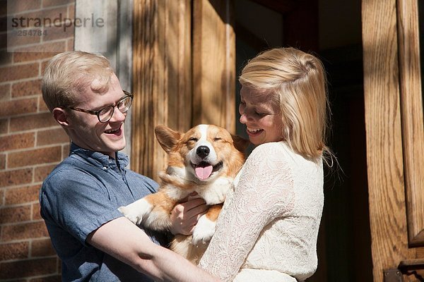 Glückliches junges Paar mit Corgi-Hund im Arm vor der Haustür