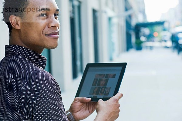 Junger Mann auf der Stadtstraße mit digitalem Tablett und Blick über die Schulter
