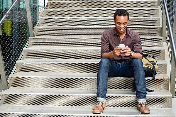 Junger Mann beim SMSen auf dem Smartphone auf der Stadttreppe