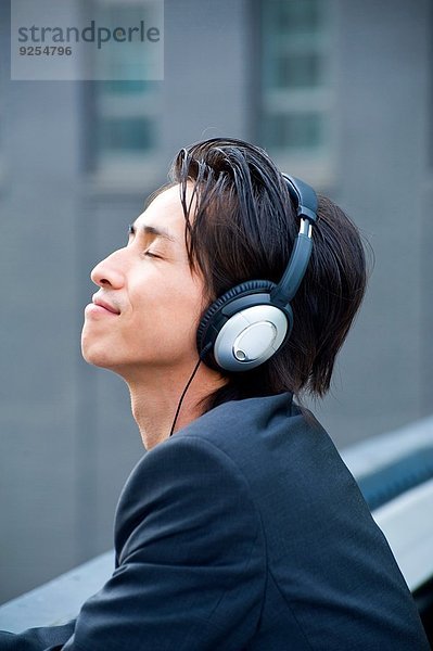 Mittlerer erwachsener Geschäftsmann auf dem Dach der Stadt  der Musik über Kopfhörer hört.