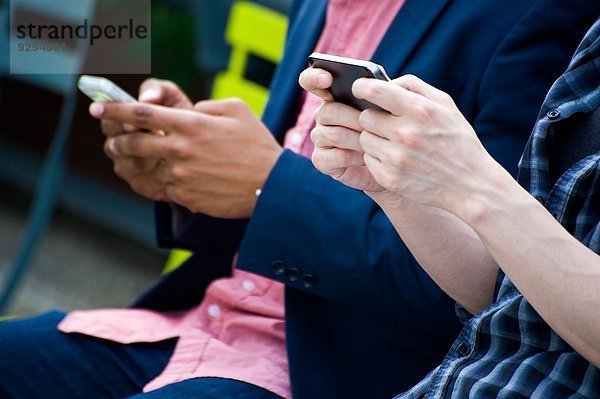 Cropped Torso Schuss von jungen Geschäftsleuten im Stadtpark SMS auf Smartphones