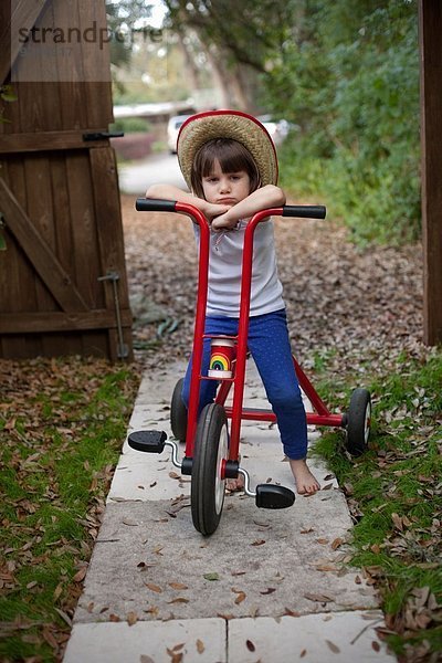 Porträt eines vierjährigen Mädchens  das auf seinem Dreirad im Garten sitzt.