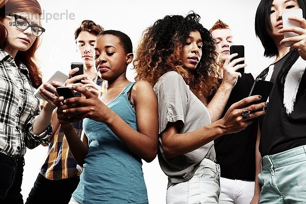 Niederwinkel-Studioaufnahme von sechs jungen Erwachsenen  die auf dem Smartphone texten.
