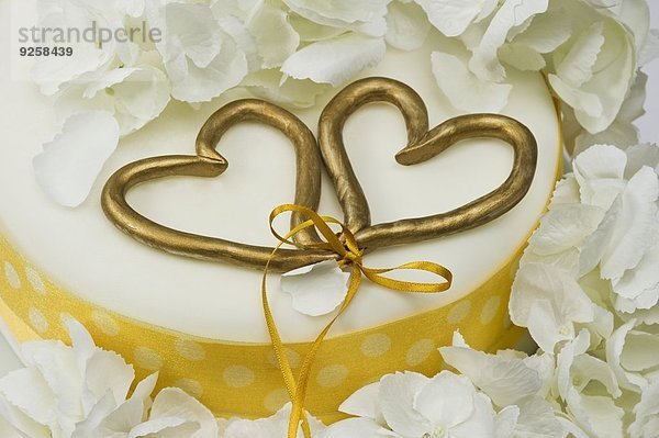 Hochzeitstorte mit zwei goldenen zusammengebundenen Herzen (Close Up)
