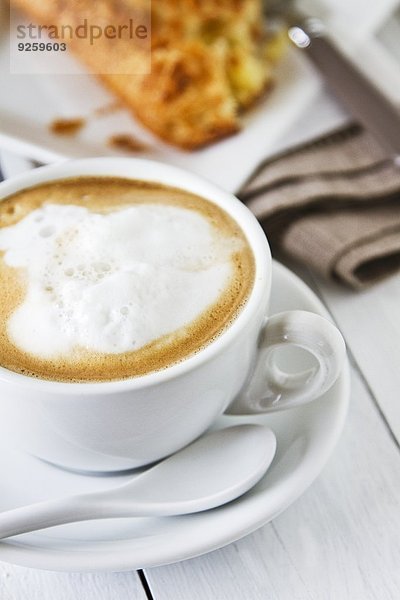 Cappuccino in Tasse mit Milchschaum  dahinter Apfeltasche