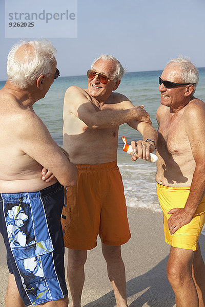 Senior Senioren eincremen verteilen Mann Strand Sonnencreme auftragen
