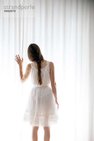 Junge Frau berührt einen weißen Vorhang  Rückansicht
