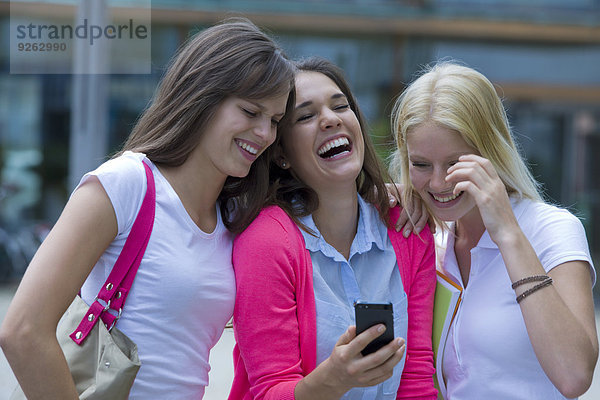Deutschland  Baden-Württemberg  Porträt von drei lachenden jungen Studentinnen mit Smartphone