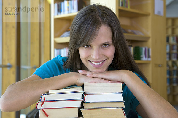 Deutschland  Baden-Württemberg  entspannte junge Studentin mit Bücherstapel in einer Bibliothek