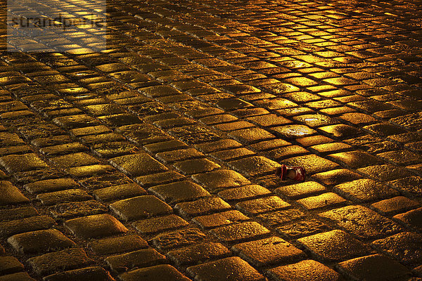 Verlorener roter Schuh liegt nachts auf nassem Bürgersteig