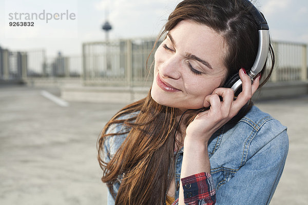 Deutschland  Nordrhein-Westfalen  Köln  Portrait einer lächelnden jungen Frau beim Musikhören mit Kopfhörern