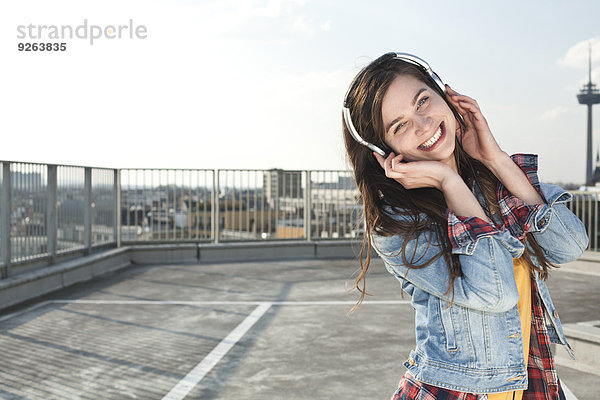 Deutschland  Nordrhein-Westfalen  Köln  Portrait einer lachenden jungen Frau beim Musikhören mit Kopfhörern