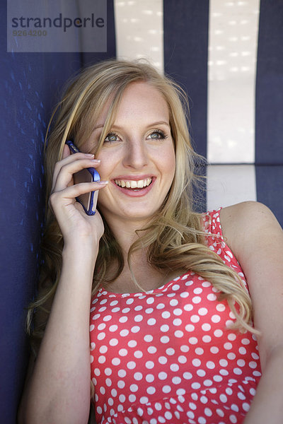 Porträt einer lächelnden jungen Frau beim Telefonieren mit dem Smartphone