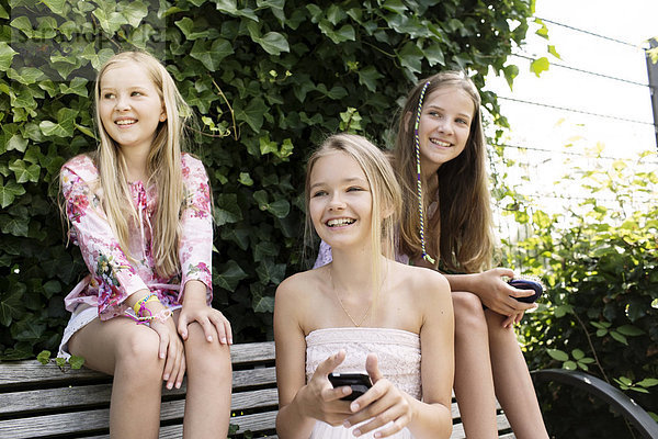 Drei lächelnde Mädchen sitzen auf einer Parkbank.