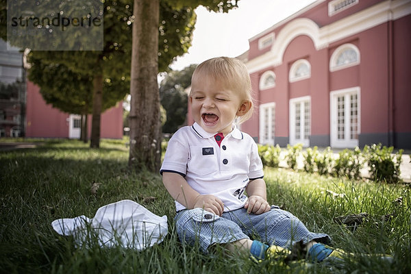 Deutschland  Oberhausen  Blonder Junge sitzend im Park von Schloss Oberhausen
