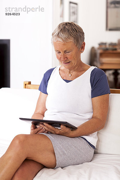 Seniorin auf der Couch sitzend mit digitalem Tablett