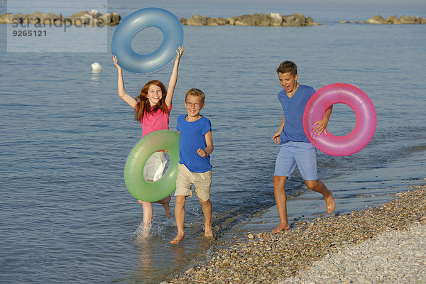 Drei Kinder  die mit ihren schwimmenden Reifen am Wasser von Adria rennen.