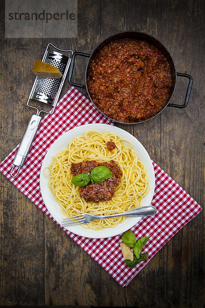 Teller Spaghetti Bolognese  Kochtopf mit Bolognese-Sauce  Parmesan  Reibe und Tuch auf dunklem Holz  erhöhte Ansicht