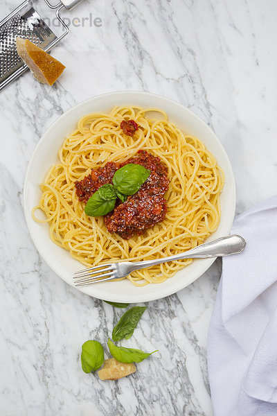 Teller Spaghetti Bolognese  Tuch  Parmesan und Basilikumblätter auf weißem Marmor  erhöhte Ansicht