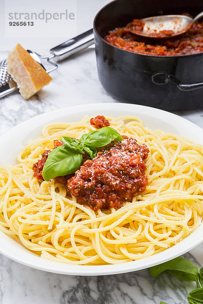 Teller Spaghetti Bolognese verziert mit Basilikumblättern auf weißem Marmor