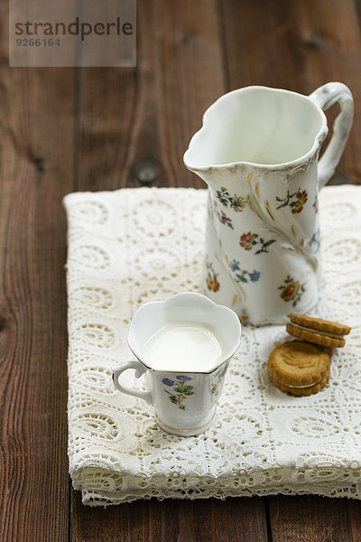 Tasse Milch  Milchkanne und Kekse auf weißer Tischdecke