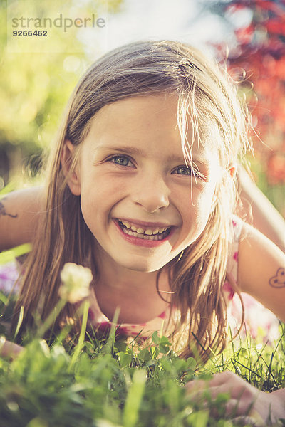 Porträt eines lächelnden kleinen Mädchens auf einer Wiese im Garten liegend