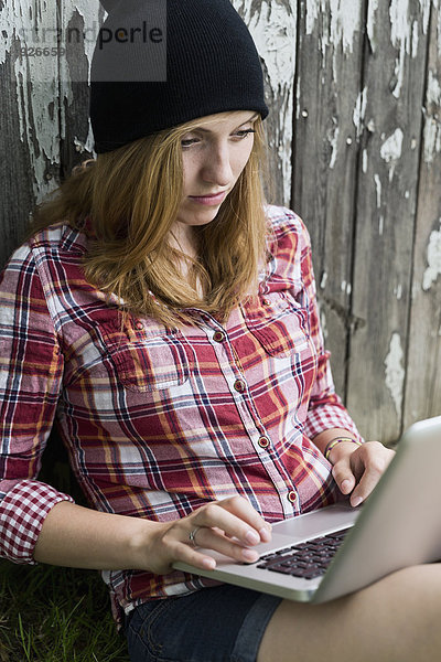 Portrait einer jungen Frau mit Laptop vor einer Holzwand