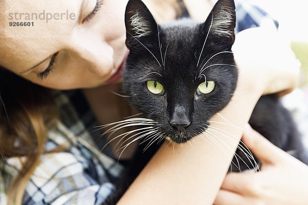 Junge Frau mit schwarzer Katze auf den Armen  Teilansicht
