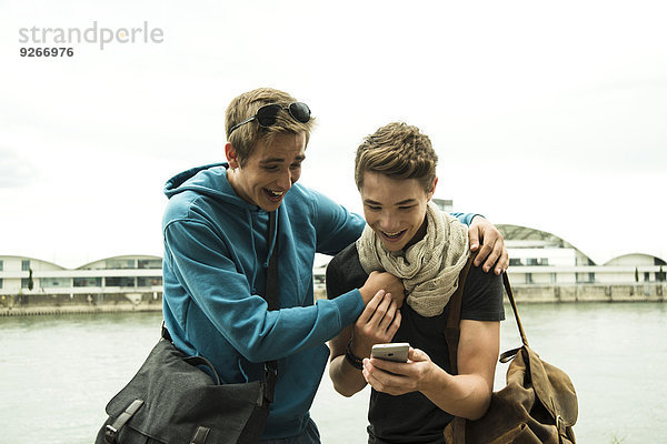 Zwei glückliche Freunde mit Handy am Flussufer