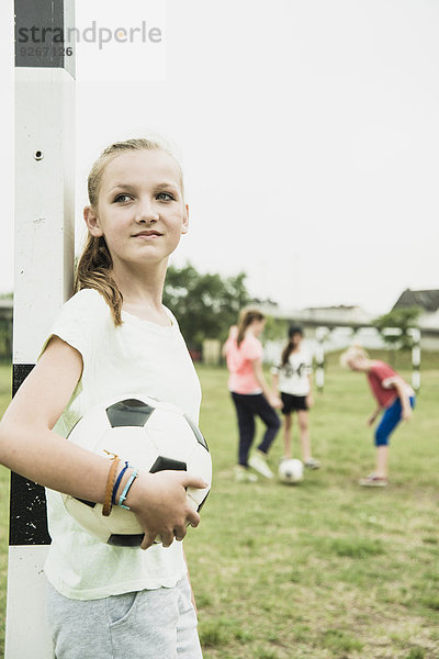 Porträt eines lächelnden Teenagermädchens mit Fußballball am Torpfosten