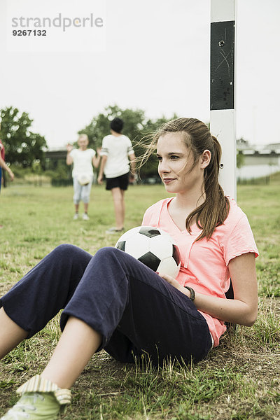 Porträt eines lächelnden Teenagermädchens mit Fußballball am Torpfosten