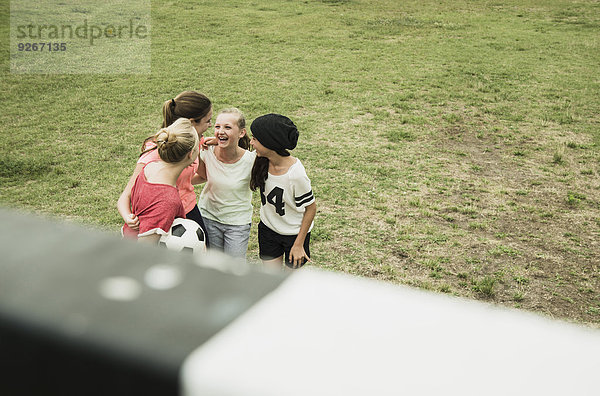 Vier weibliche Teenager-Freunde  die sich auf einem Fußballfeld amüsieren.