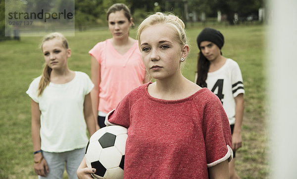 Porträt eines ernsthaft aussehenden Teenagermädchens mit Fußball vor drei anderen Mädchen