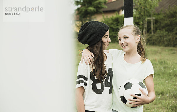 Zwei fröhliche Teenager-Mädchen stehen auf einem Fußballplatz