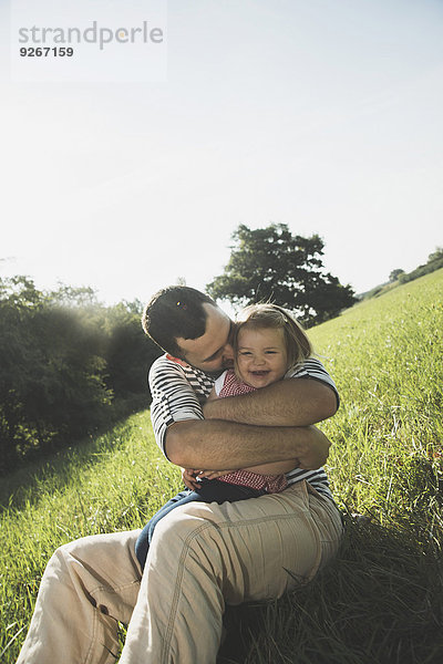 Vater umarmt seine lachende kleine Tochter auf einer Wiese
