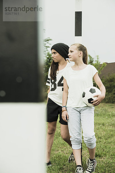 Zwei Teenagermädchen mit Fussball auf einem Fussballplatz stehend