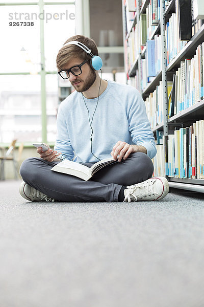 Student in einer Universitätsbibliothek auf dem Boden sitzend mit Kopfhörer