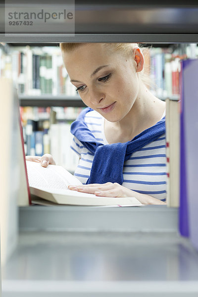 Student in einer Universitätsbibliothek Lesebuch am Regal