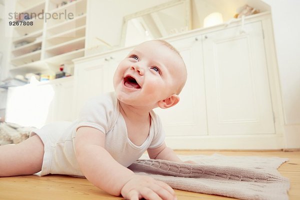 Lächelnder kleiner Junge  der auf dem Boden des Wohnzimmers krabbelt.