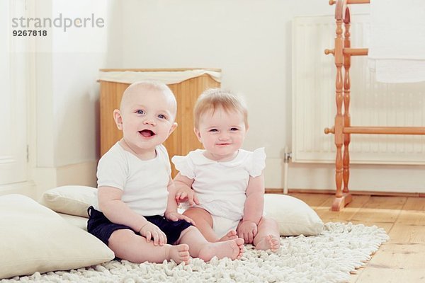 Porträt eines lächelnden Mädchens und eines Jungen  die auf einem Teppich sitzen.